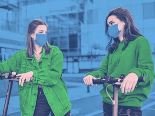 Two girls in green shirts leaning on their electric scooters while wearing masks during the pandemic...