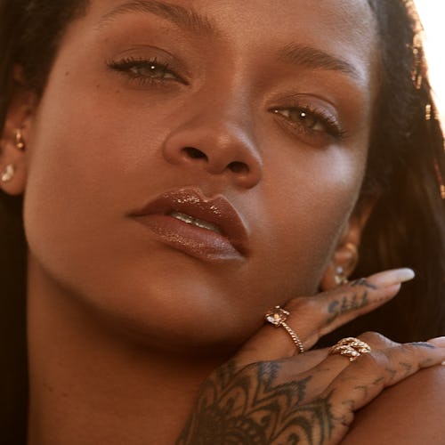A closeup of Rihanna with her hand on her shoulder, covered in henna 