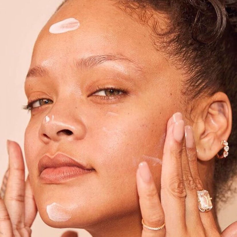 A closeup of Rihanna applying a cream from her Fenty Skin brand 
