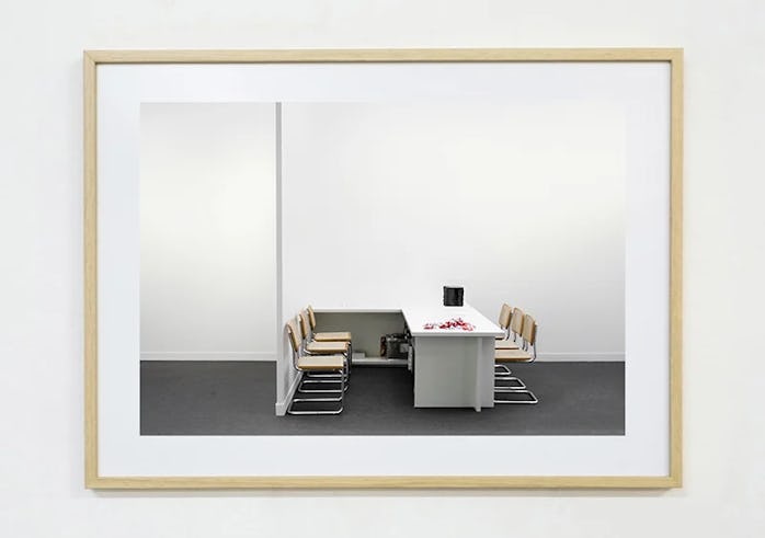 A sterile white room can be seen. It has six beige chairs place in line around a white table. 