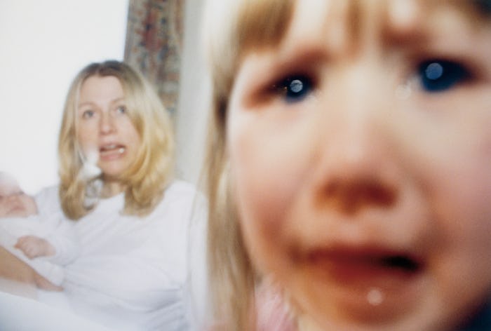 A mother holds a baby and a toddler looks at camera.