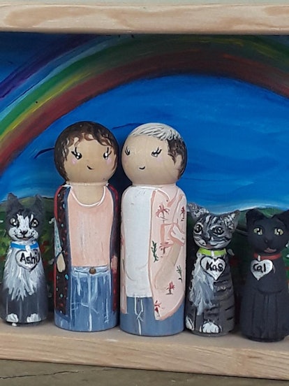 Two peg doll people are displayed with three peg doll cats with a rainbow and landscape background.