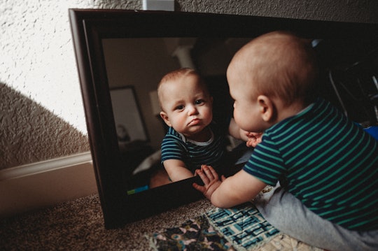 A baby looks at his reflection in a mirror.