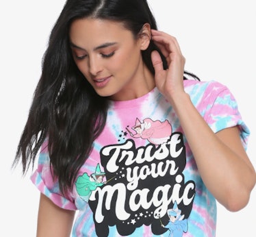A woman with long brown hair looks down while wearing a tie-dye Disney tee.