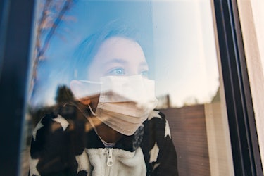 A girl with face mask looking through a window 
