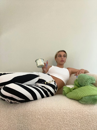 Internet personality Emma Chamberlain lying down on a bed wearing a white crop top and black and whi...