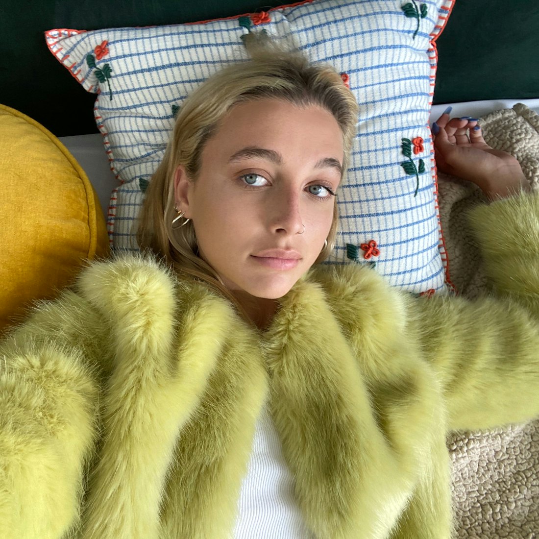 Internet personality Emma Chamberlain lying down on a bed wearing yellow fur coat