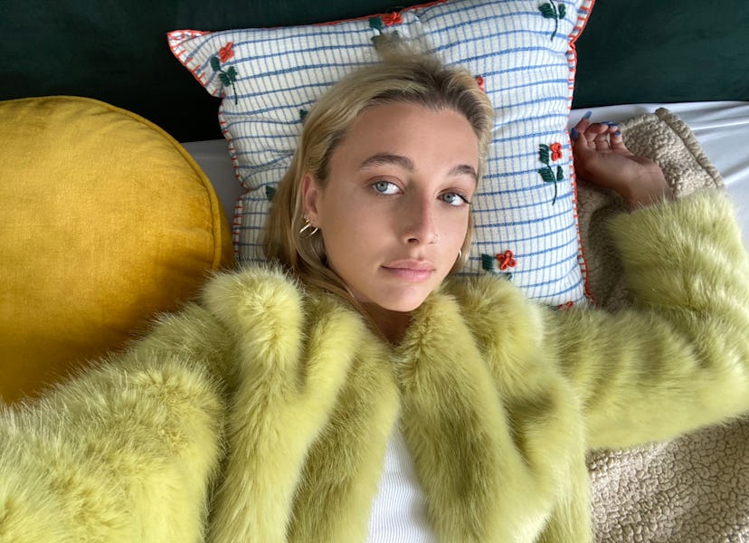 Internet personality Emma Chamberlain lying down on a bed wearing yellow fur coat