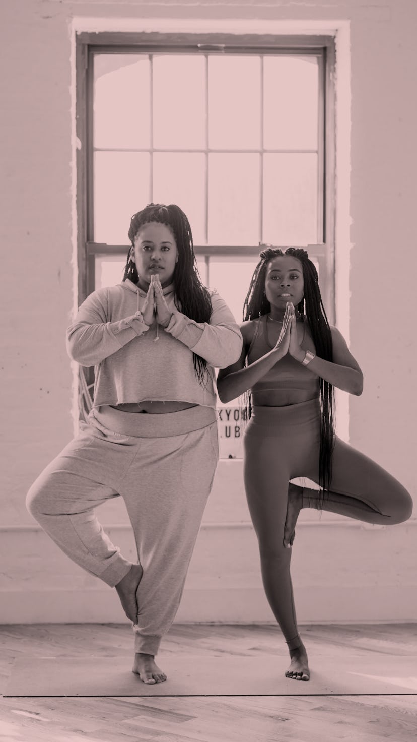 Two women holding a standing yoga pose in the fitness class in front of a window