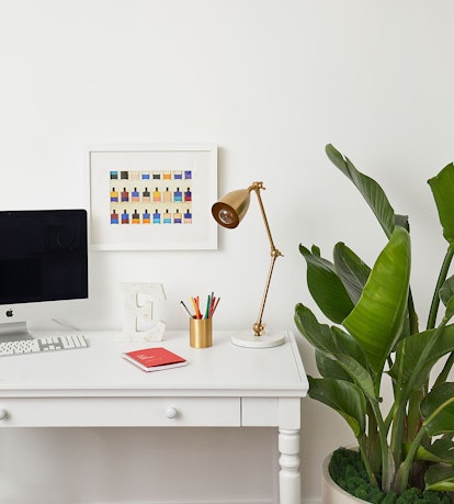A remote learning set-up features a minimalistic desk, gold lamp, computer, and plants, created with...