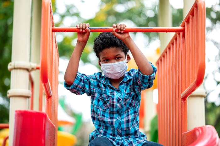 A boy wearing a mask sits on playground equipment.