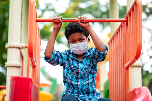 A boy wearing a mask sits on playground equipment.