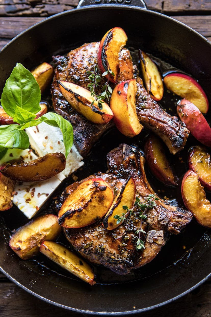 A cast iron skillet filled with glazed peaches and pork chops.