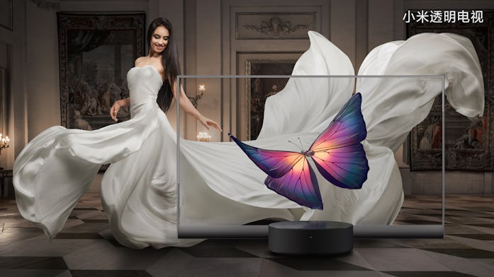 A model in a white dress is seen behind a transparent Xiaomi TV screen. The model can be seen in an ...