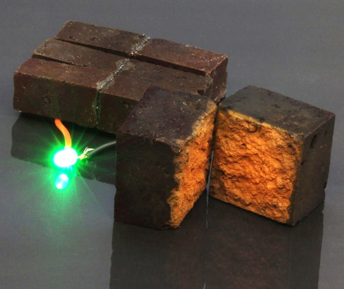 Three red bricks can be seen. A green LED light emerges from one of them, fully lit without any othe...