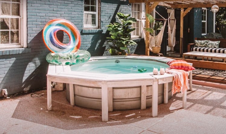 A decorated stock tank pool sits in the backyard with pool floats and cocktails.
