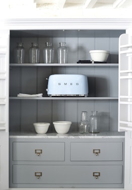 A light blue SMEG toaster sits in a cabinet with minimalistic vases and plates.