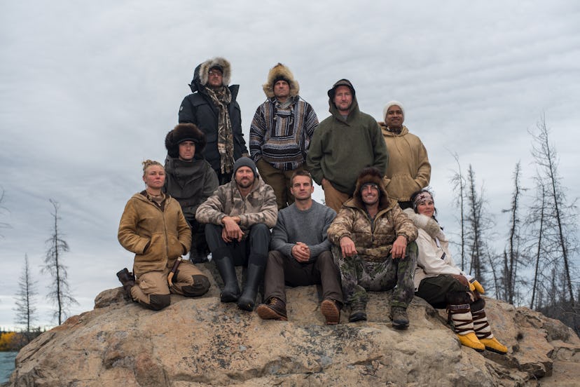 10 outdoorsy competitors sit on a rock in the Arctic.