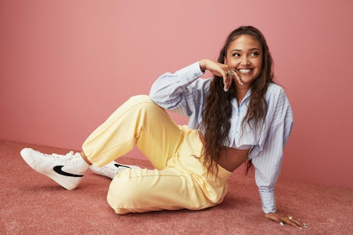 Joy Crookes pictured wearing a blue shirt, yellow trousers, and black and white Nike blazers against...