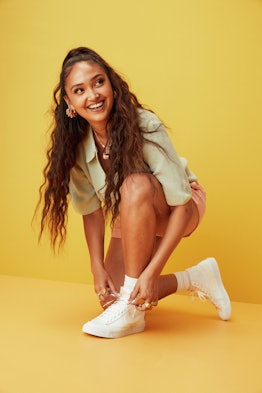 Joy crookes poses with white Nike blazer trainers against a yellow background