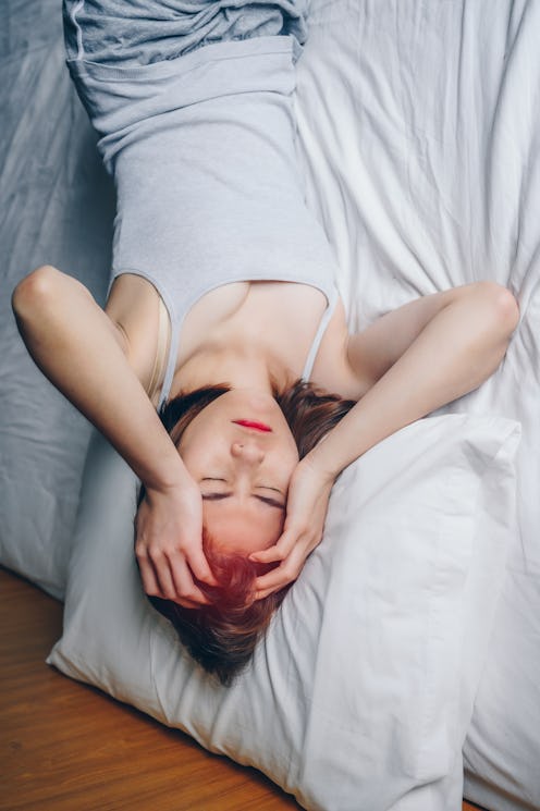 A woman with dyed red hair holds her head while hungover. Doctors explain how a white claw hangover ...