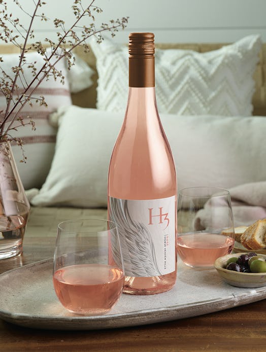 A bottle of H3 Wines' rosé sits on a ceramic serving dish in a living room with two full glasses and...