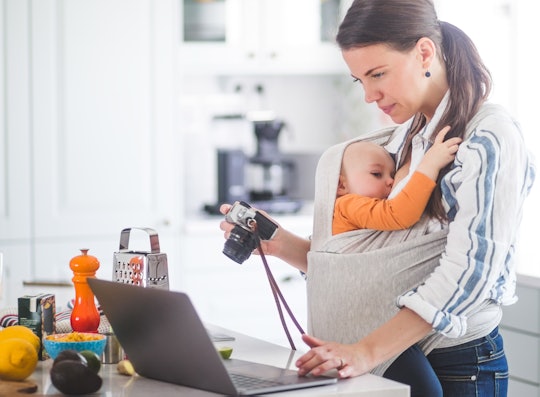 mom breastfeeding baby in a baby carrier while working on her laptop