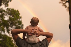 baby sitting on parent's shoulders watching rainbow