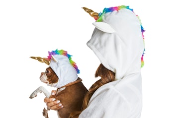 A woman, in a unicorn costume, holds her dog, who is also in a unicorn costume. 
