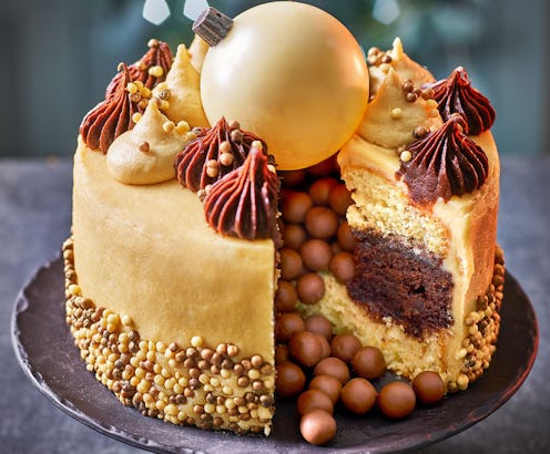 A gold coloured cake with chocolate decorations and a giant white chocolate christmas bauble on top