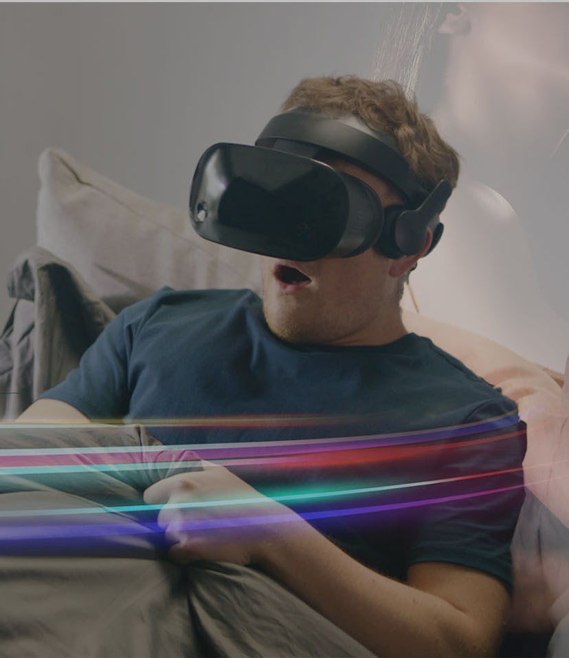 A man wearing a VR headset in bed reaching beneath his covers.