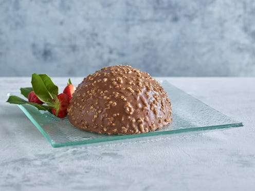 A milk chocolate dome covered in hazelnut pieces on a glass plate