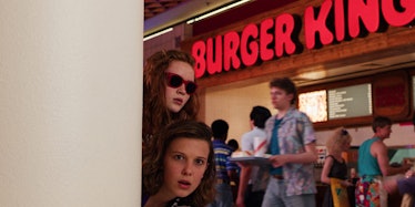 Eleven and Max in Netflix's 'Stranger Things' poke their head around a wall in the Starcourt Mall.
