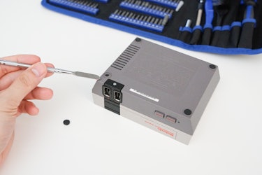 Use a pry tool pop off these four rubber pads to reveal the hidden screws to open up the NES Classic...