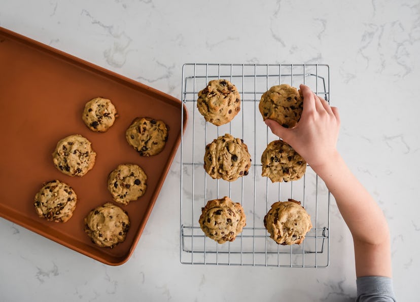 child grabbing fresh chocolate cookie from cooling rack for after-school snack