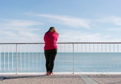 A woman leaned on the fence and looking at the sea experiencing anxiety in summer 