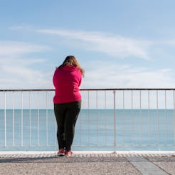 A woman leaned on the fence and looking at the sea experiencing anxiety in summer