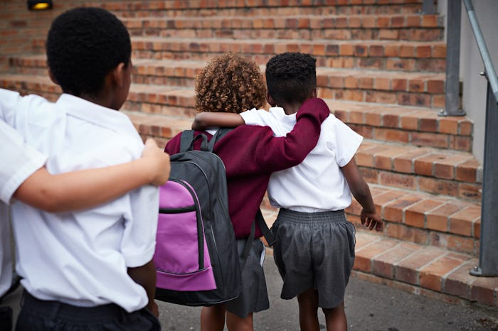 Three children in uniform walking into school with arms over shoulders