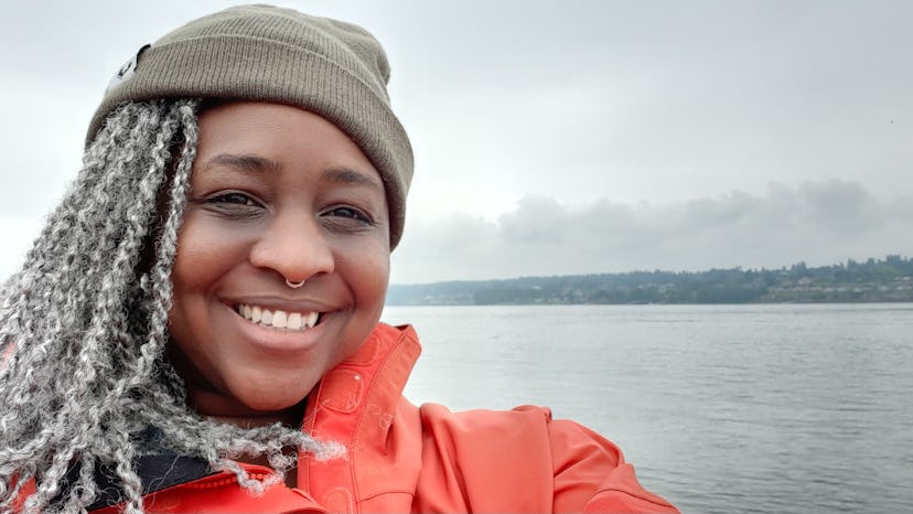 Mercy Shammah in an orange jacket taking a selfie outdoors with a sea in the background
