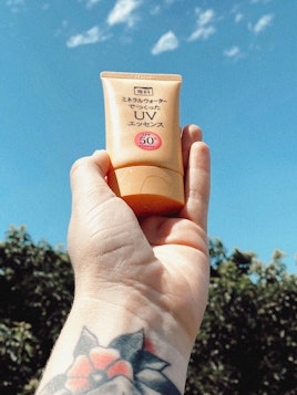 A hand holding Shiseido Senka Aging Care UV Sunscreen product