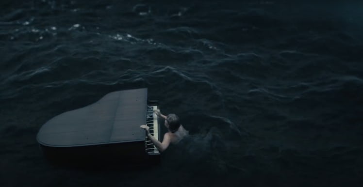 Taylor Swift holds onto a piano that's floating in the middle of a rough ocean in her "cardigan" mus...