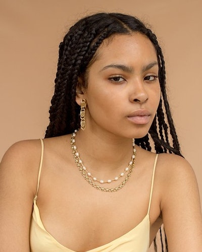 A woman in a vanilla top with a thick chain necklace and a pearl necklace and chain earrings