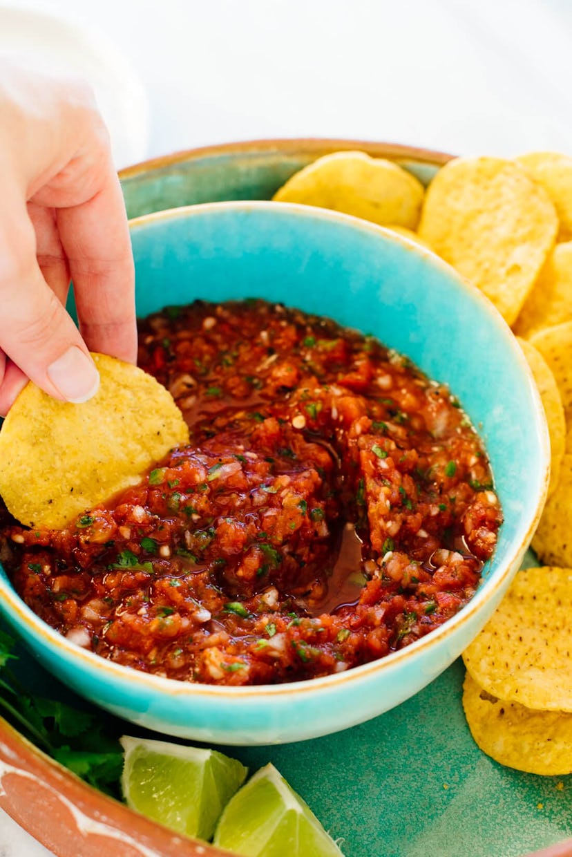 hand dipping a tortilla chip into a blue bowl of fresh salsa