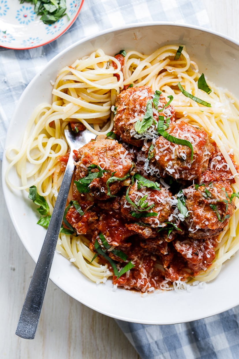 Meatballs covered in red sauce served on top of spaghetti in white bowl