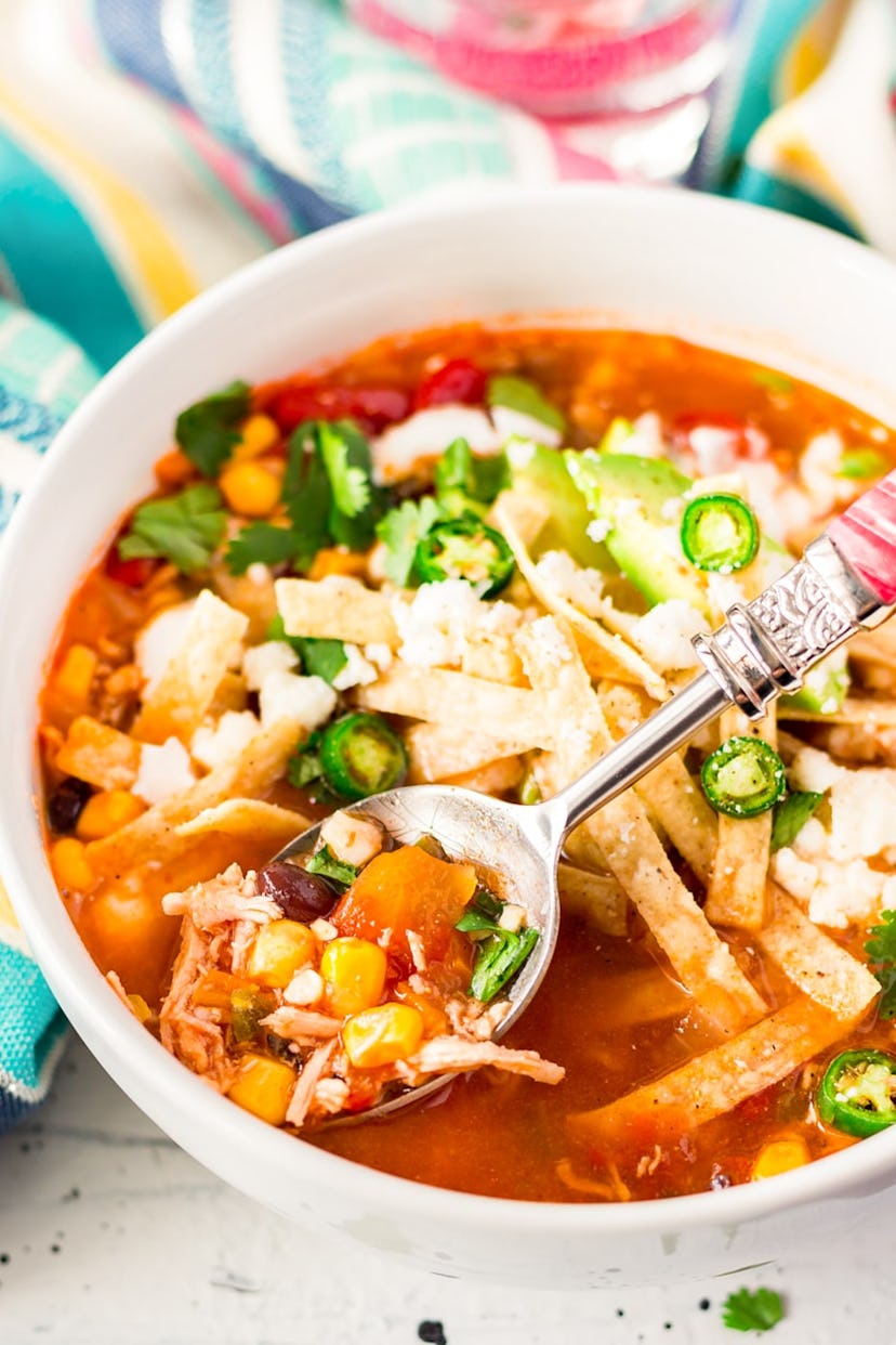 white bowl full of tortilla soup with a spoon coming out of it, holding a spoonful of the soup
