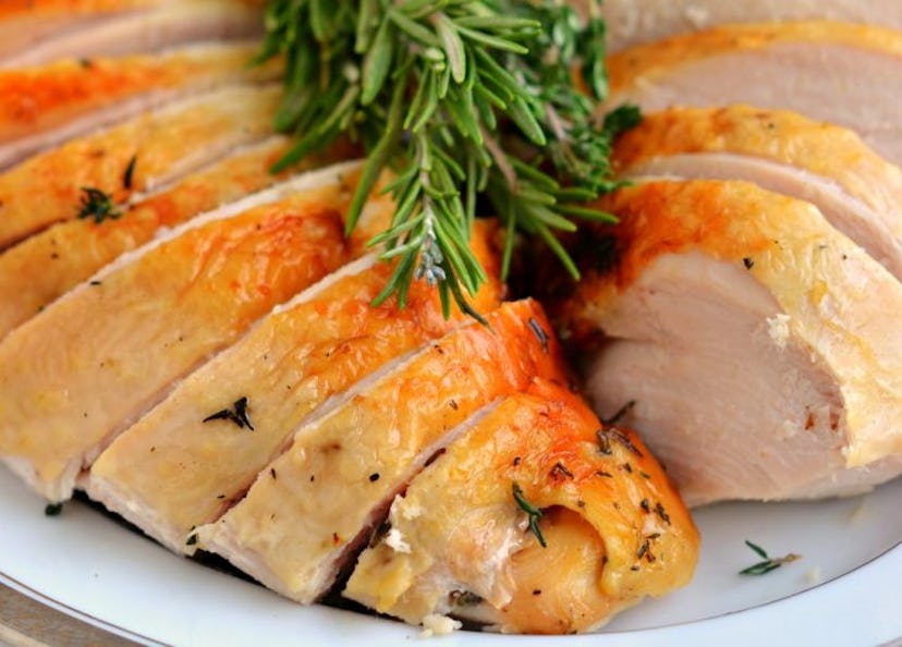 Two slices of turkey breast with herbs and a green garnish on a white plate