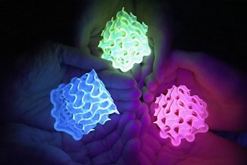 Three pairs of hands can be seen holding bright neon green, blue, and pink fluorescent lights in the...