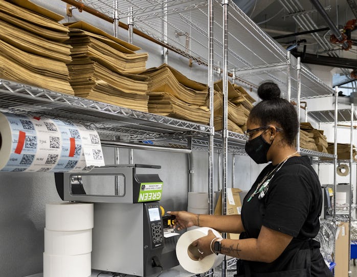 A young woman wearing a face mask is seen issuing a receipt through a machine. There are empty boxes...