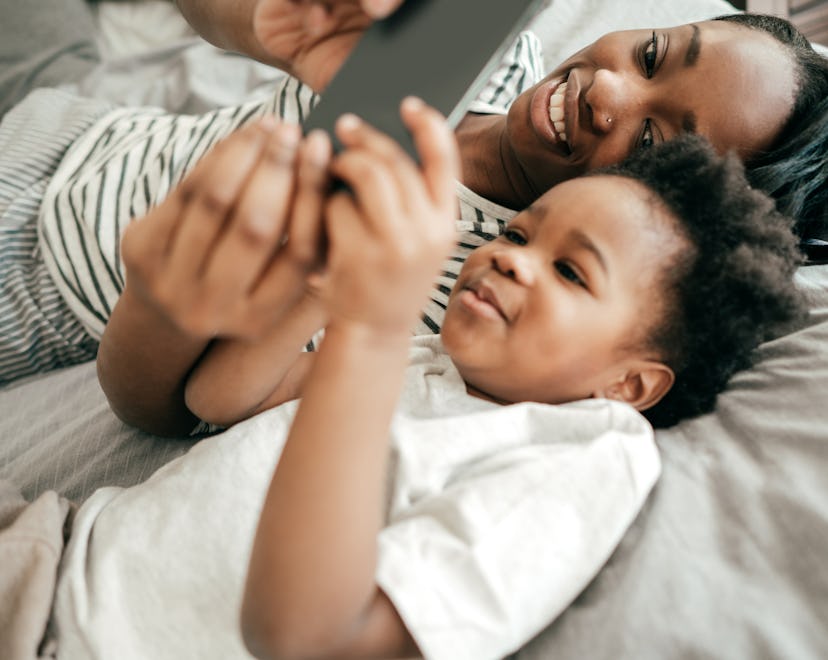 A toddler boy using an app on his iPhone while lying next to his mother