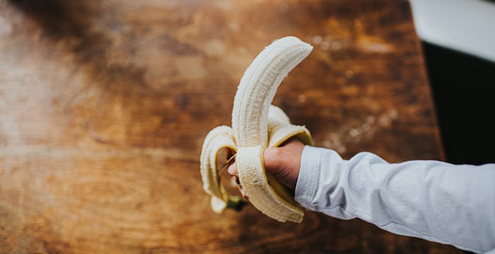 A childs hand holds an peeled banana with a bit taken out of it on a wooden table